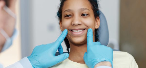 Portrait of teen black girl with toothy smile sitting in a dental chair at dentistry clinic