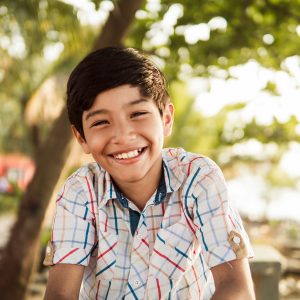 Happy Young Boy Smiling in a Sunny Outdoor Setting A portrait of a cheerful young boy with a beaming smile, enjoying a sunny day outdoors with a blurred background.